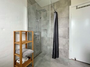 A modern bathroom with a glass shower enclosure, a wooden shelf with towels, and a door with a towel rack. - Charming holiday apartment in central Stege (Stege)