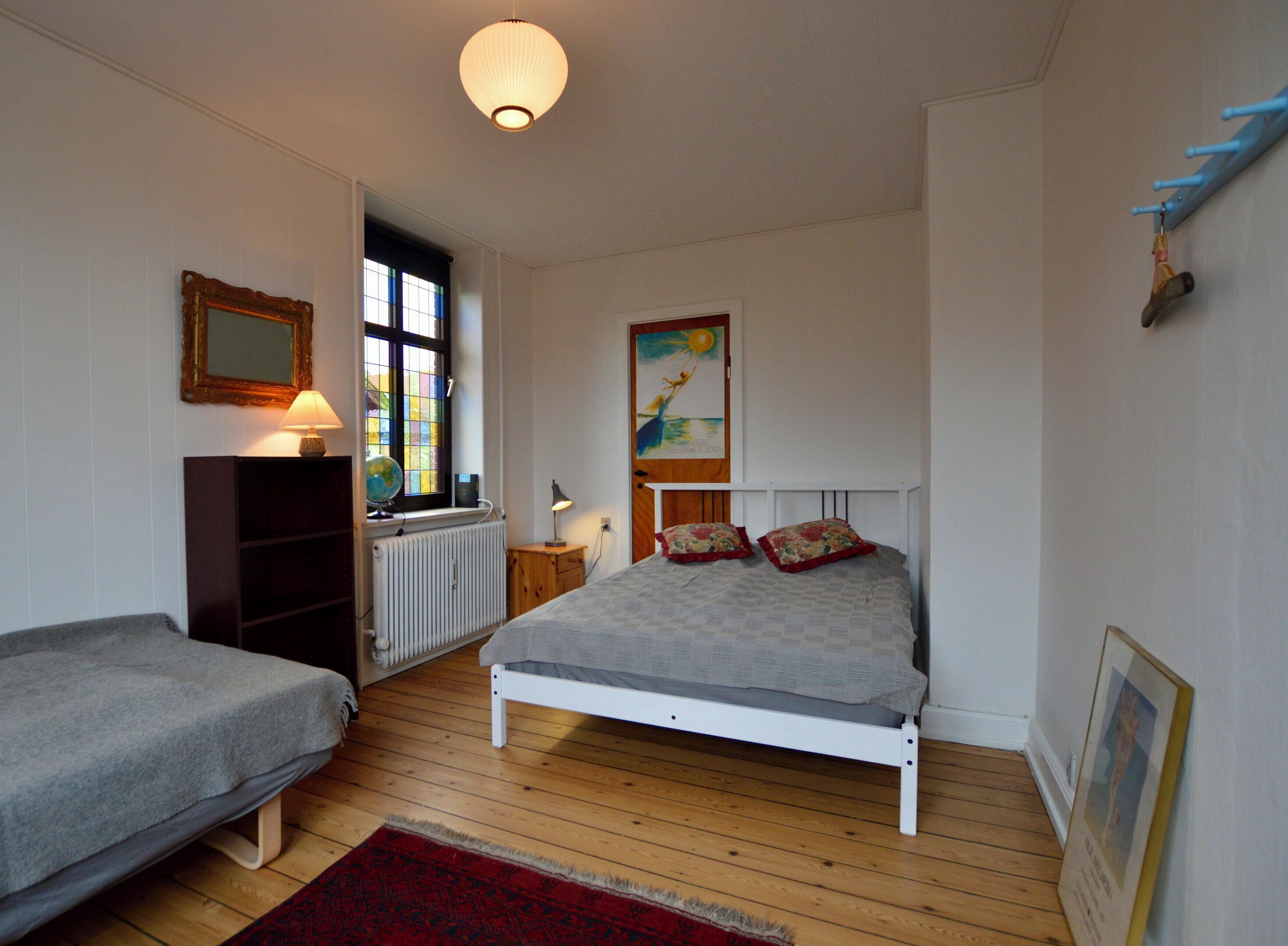 Un dormitorio con cama, ventana, radiador, un globo terráqueo y un cuadro en la pared.