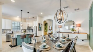 A modern kitchen with a central island, stainless steel appliances, and a dining area with a long table set for six.