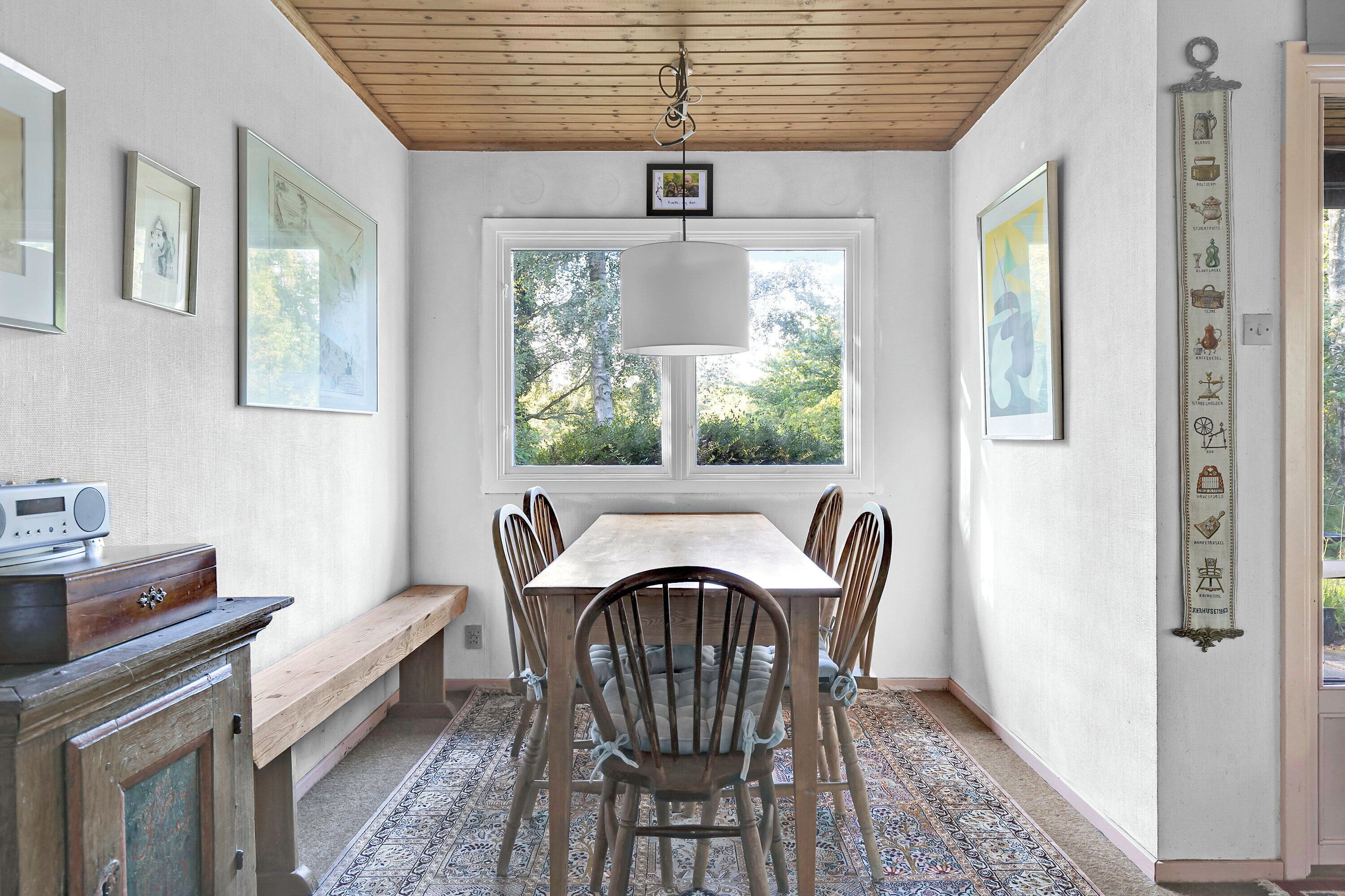 Un espace repas comprenant une table en bois, des chaises, un banc, un luminaire suspendu et des œuvres d’art encadrées accrochées aux murs.
