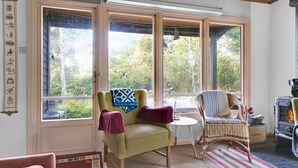 A cozy room with a large window, a chair, a small table, and a wood-burning stove. - Cottage by Veddinge in charming 70s style (Fårevejle)