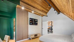 Una camera da letto con soffitto in legno, un letto, una TV a parete e una panca di legno.
