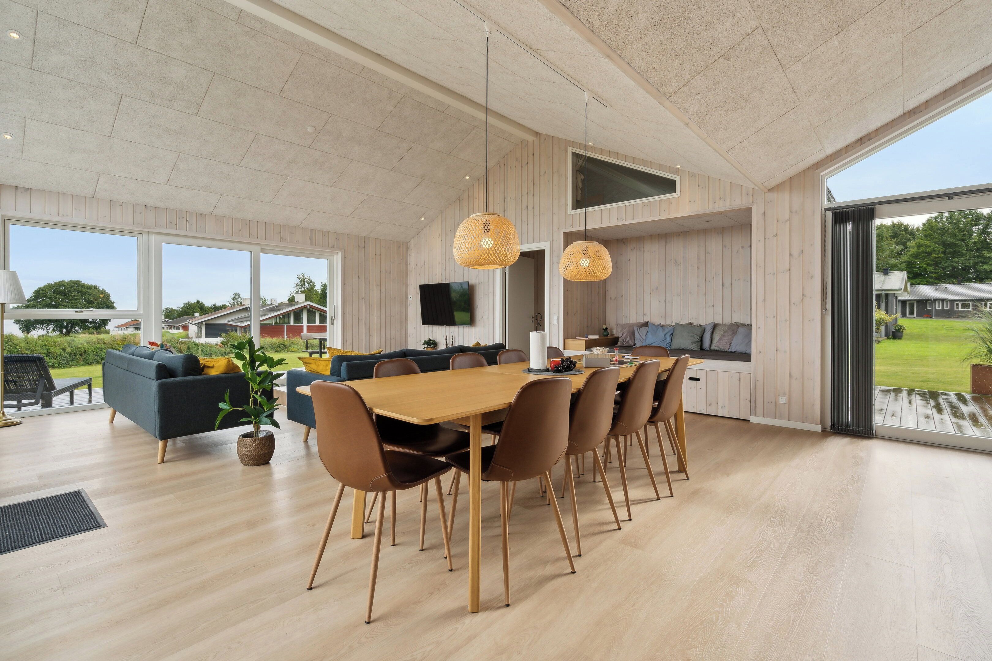 Ein geräumiger Essbereich mit einem langen Holztisch und modernen Stühlen, eine gemütliche Sitzecke mit Sofas und große Fenster mit Blick ins Freie.