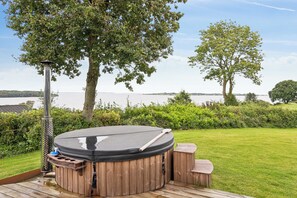 A hot tub on a wooden deck with a view of a lake and trees.