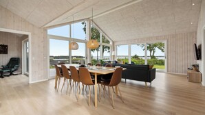 A spacious dining area with a wooden table and chairs, large windows offering a view of the outdoors, and a modern interior design. - Lovely, new-built cottage near sea (Aabenraa)