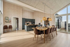 Une cuisine spacieuse aux murs en bois, un coin repas avec une grande table et des chaises, et une vue dégagée grâce à de grandes fenêtres.