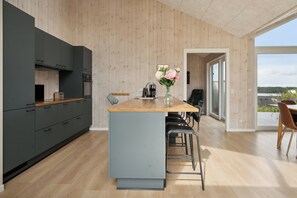 A modern kitchen with a wooden island, black cabinets, and a view to the outside. - Lovely new-built cottage near sea (Aabenraa)