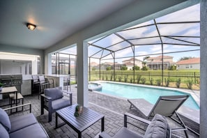 En overdækket udendørs terrasse med swimmingpool, grillområde og siddepladser.