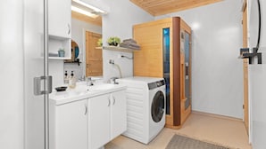 Un baño moderno y funcional con lavadora integrada, lavabo con espejo y detalles de madera en el techo y las paredes.