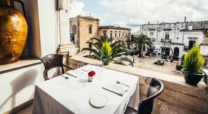 A dining table set with a white tablecloth, plates, and cutlery, overlooking a courtyard with buildings and palm trees. - Panoramic balcony - Quiet location - Parking 200 m away - Air conditioning (Ostuni)