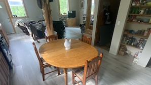 A spacious dining area with a wooden table and chairs, a ceiling with exposed beams, and a view of the outdoors through a window. - Private house on wooded acreage (Talkeetna)
