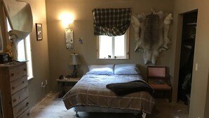 A bedroom with a large bed, a dresser, a window, a lamp, and a mounted animal hide. - Private house on wooded acreage (Talkeetna)