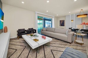 Uma sala de estar moderna com um sofá branco, duas poltronas pretas, uma mesa de centro branca e um tapete estampado.