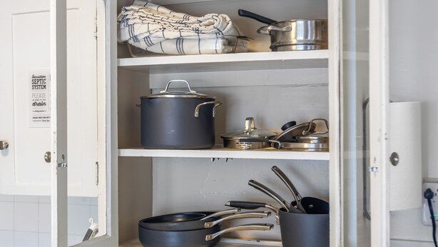 A kitchen cabinet with pots, pans, and a folded cloth.