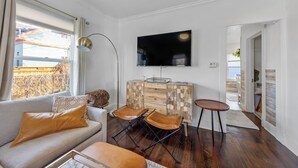 A living room with a sofa, two leather chairs, a wooden cabinet, and a flat-screen TV mounted on the wall.