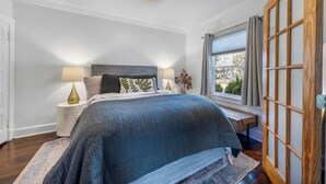 A bedroom with a large bed, bedside lamps, a window with curtains, and a view of the outdoors.