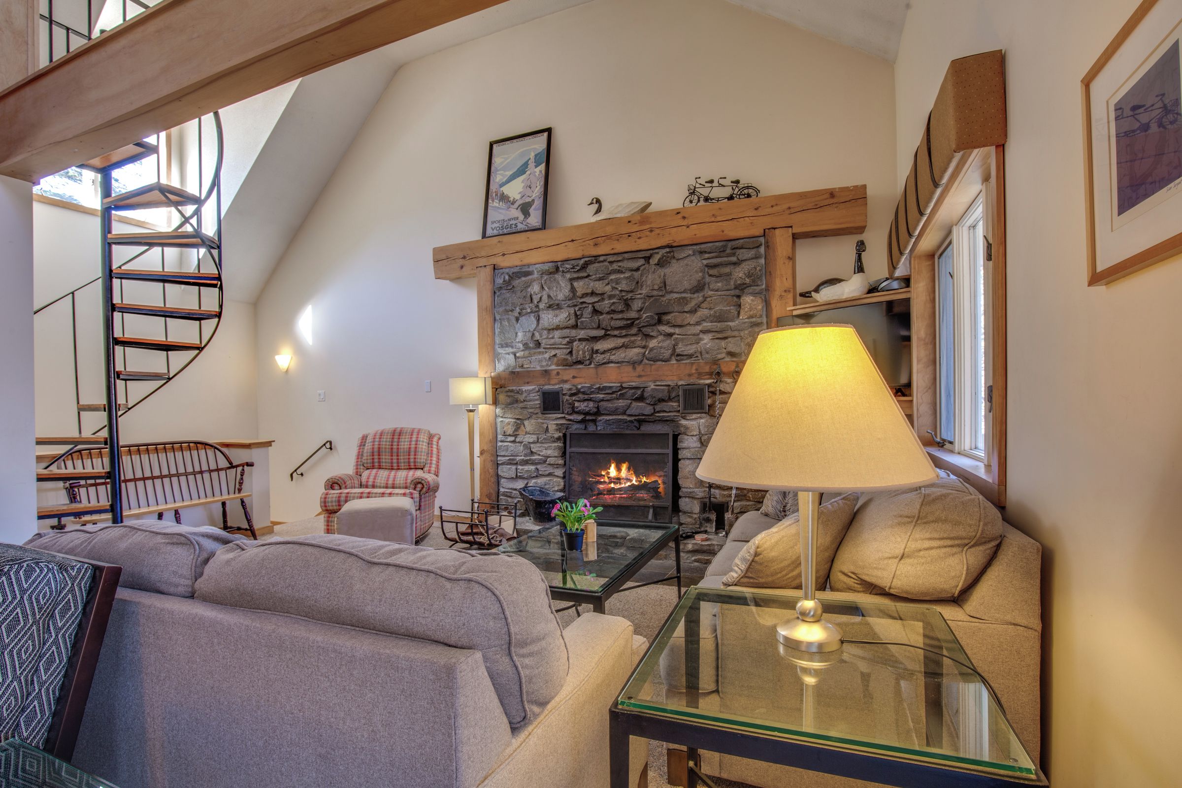 A cozy living room with a stone fireplace, a spiral staircase, and a comfortable seating area.