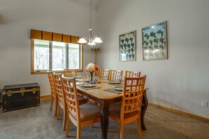 A dining area with a wooden table set for six, surrounded by wooden chairs. There is a black trunk on the floor to the left, and a window with blinds on the wall to the left of the table. - The Big Lift-abowski 3BA/2BA. Close to Mountain and Skiing! (Killington)