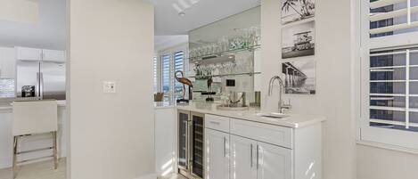 Una cocina moderna con armarios blancos, un refrigerador de acero inoxidable y un estante de vidrio.