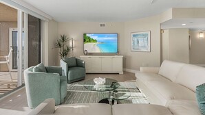 Una sala de estar moderna con un televisor de pantalla plana grande, un sofá blanco, un sillón verde y una mesa de centro de vidrio.