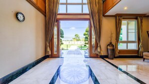A hotel lobby with a marble floor, a large window with curtains, a clock on the wall, and a view of the outside. - Luxury 6 Bed Mansion - CAS (Cha-am)