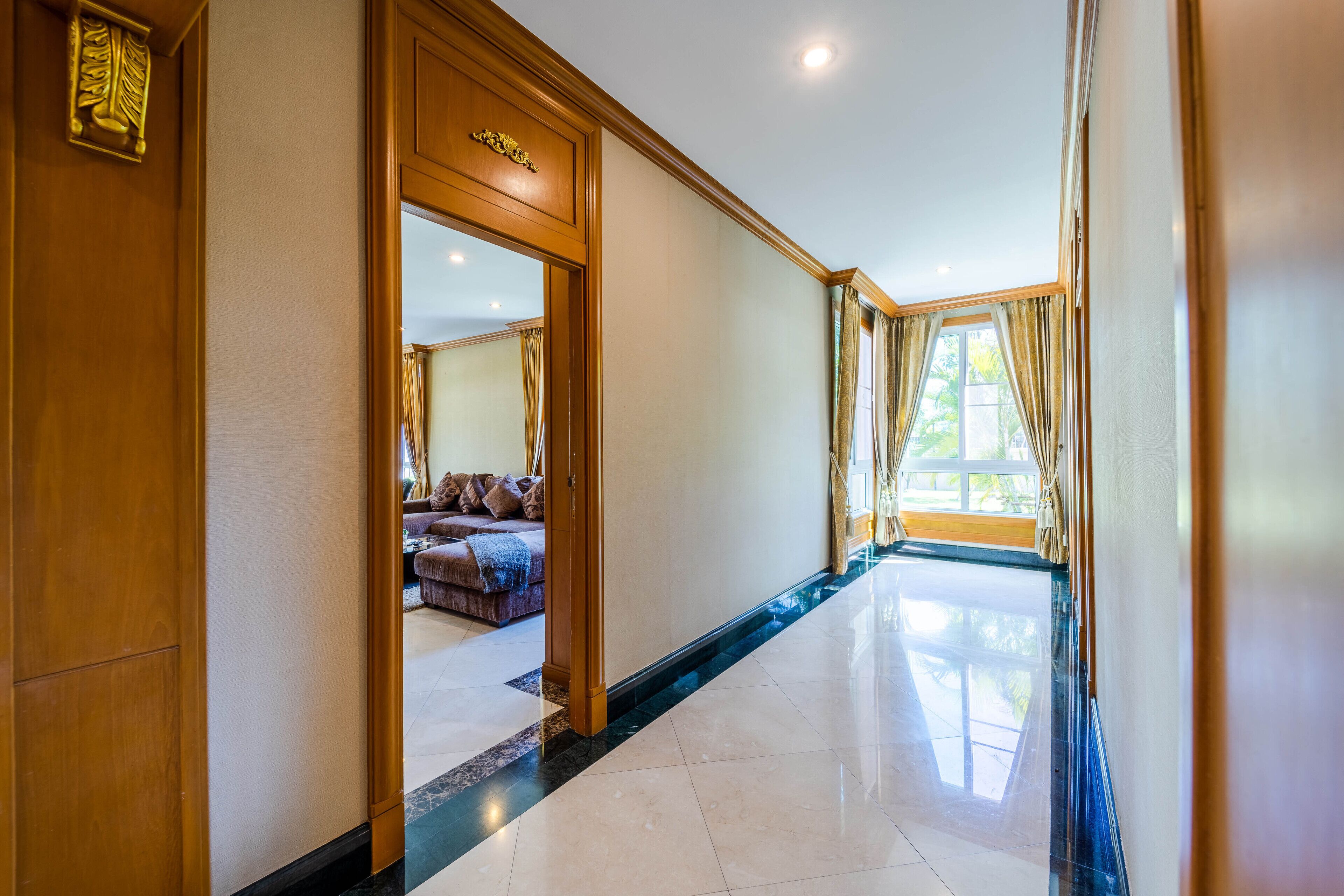 Un pasillo con una puerta de madera, un espejo y vista a una habitación con cama y cortinas.