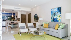 A modern living room with a grey sofa, white armchairs, a glass coffee table, and a painting of a sea creature. - 2 Bedroom Swim Up Suite Cancun (Cancun)