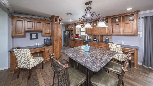 A kitchen with wooden cabinets, a granite countertop, and a chandelier. There are four chairs with patterned upholstery and a dining table.