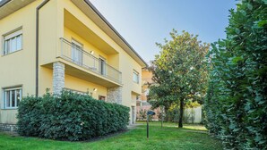 Ein gelbes Gebäude mit Balkon, umgeben von gepflegten Hecken und einem Baum.