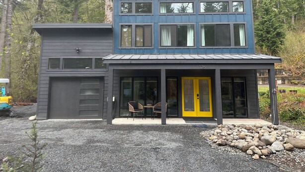Une maison moderne à deux étages, dotée d’un garage, d’une porte jaune et d’une terrasse avec des chaises.