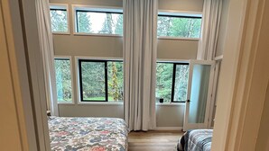 Une chambre avec un grand lit, un plus petit lit et de nombreuses fenêtres.