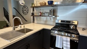 Une cuisine moderne équipée d’une cuisinière en acier inoxydable, d’un évier et d’un luminaire suspendu.