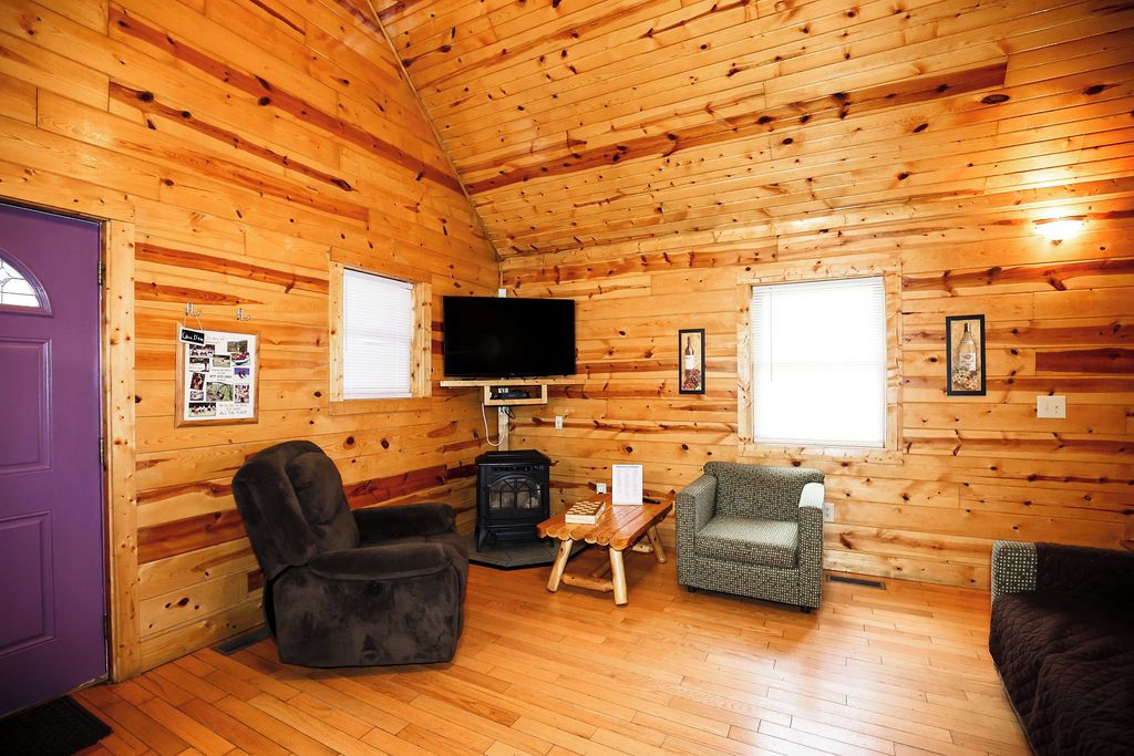 A log cabin interior with a fireplace, a television, and seating arrangements.
