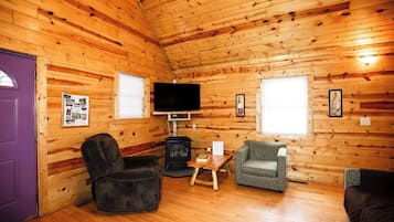 A log cabin interior with a fireplace, a television, and seating arrangements.