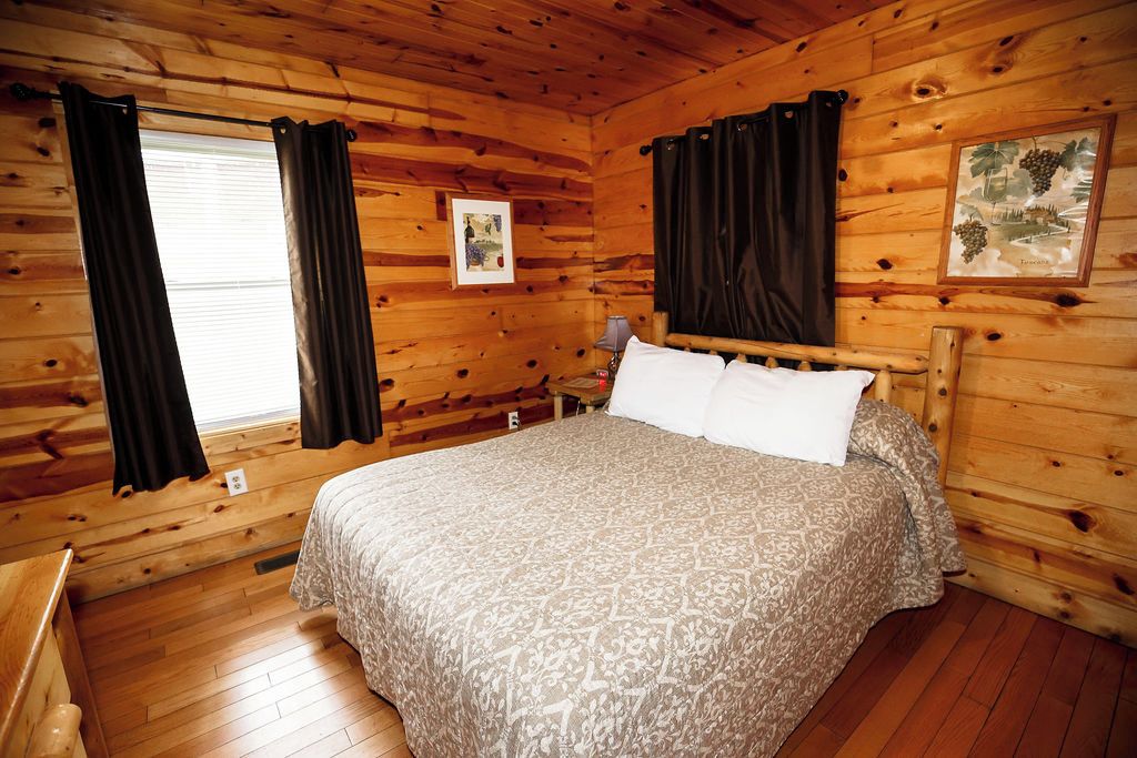 A wooden cabin room with a bed, curtains, and a framed picture on the wall.