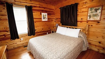 A wooden cabin room with a bed, curtains, and a framed picture on the wall.