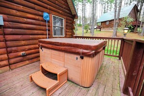 A wooden cabin with a hot tub and a wooden bench on a deck.