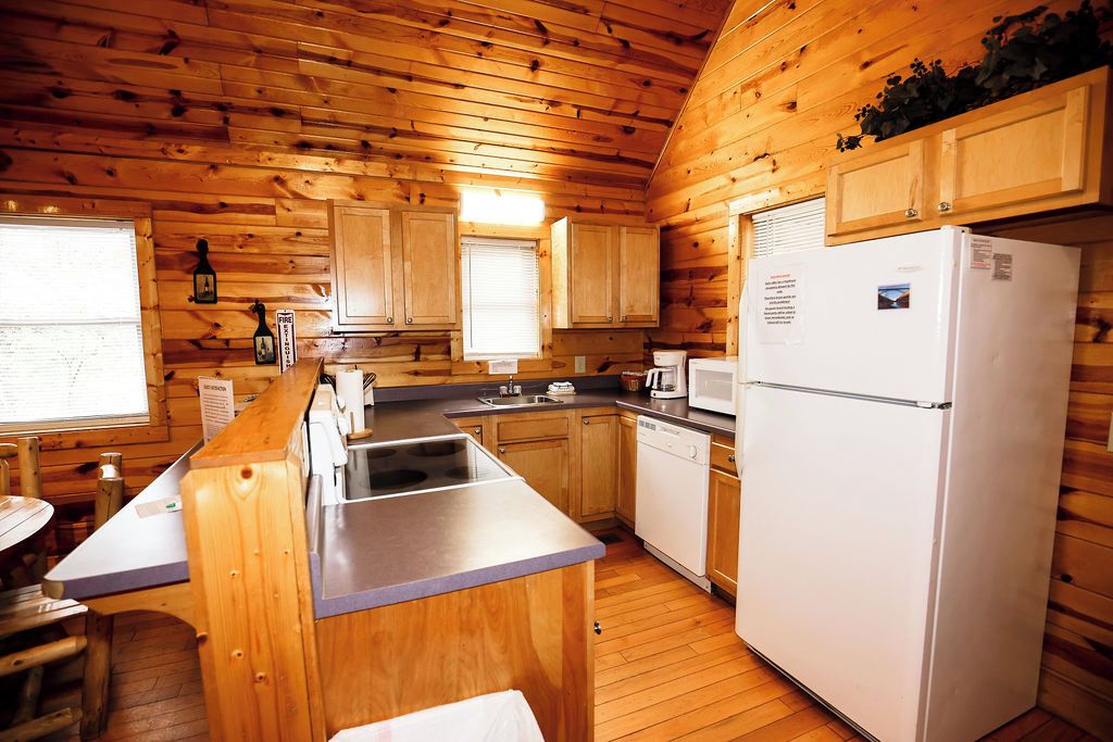 A cabin-style kitchen with wooden walls, a refrigerator, a sink, and a window.