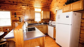 Een keuken in chaletstijl met houten wanden, een koelkast, een spoelbak en een raam.
