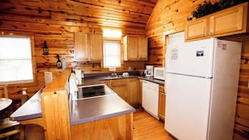 A cabin-style kitchen with wooden walls, a refrigerator, a sink, and a window.