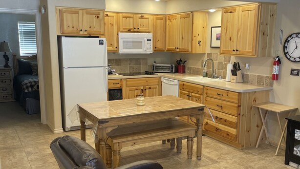 Una cocina moderna con armarios de madera, un microondas y un lavamanos. Hay una zona de comedor con una mesa y sillas.