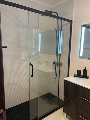 A modern bathroom with a glass-enclosed shower, a dark wooden vanity, and a mirror above the sink. - Cozy brand-new apartment in the heart of Albufeira, three minutes from the beach (Albufeira)