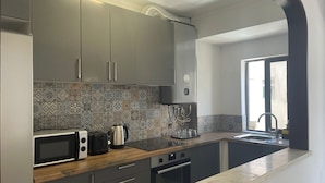 Een moderne keuken met grijze kastjes, een decoratieve spatwand, een inbouwoven en een raam met uitzicht.