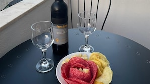 Een tafel met een fles wijn, twee glazen, een bord met salami en chips, en een stoel.