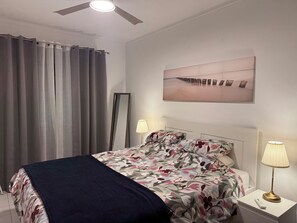 A bedroom with a bed, two bedside lamps, a ceiling fan, a large mirror, and a painting on the wall. - Cozy brand-new apartment in the heart of Albufeira, three minutes from the beach (Albufeira)