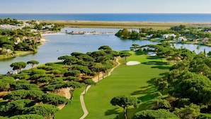 Een golfbaan met een waterpartij, bomen en een heldere lucht.