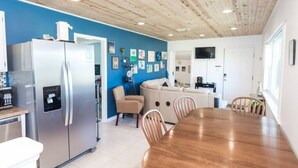 Een moderne keuken met een roestvrijstalen koelkast, een eettafel met stoelen, en een blauwe accentmuur met kunstwerken.