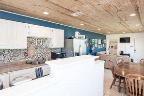 A modern kitchen with white cabinets, a tiled backsplash, and a central island. There is a dining area with a wooden table and chairs. - Pet Friendly Cheerful home on Emerald Coast (Panama City)