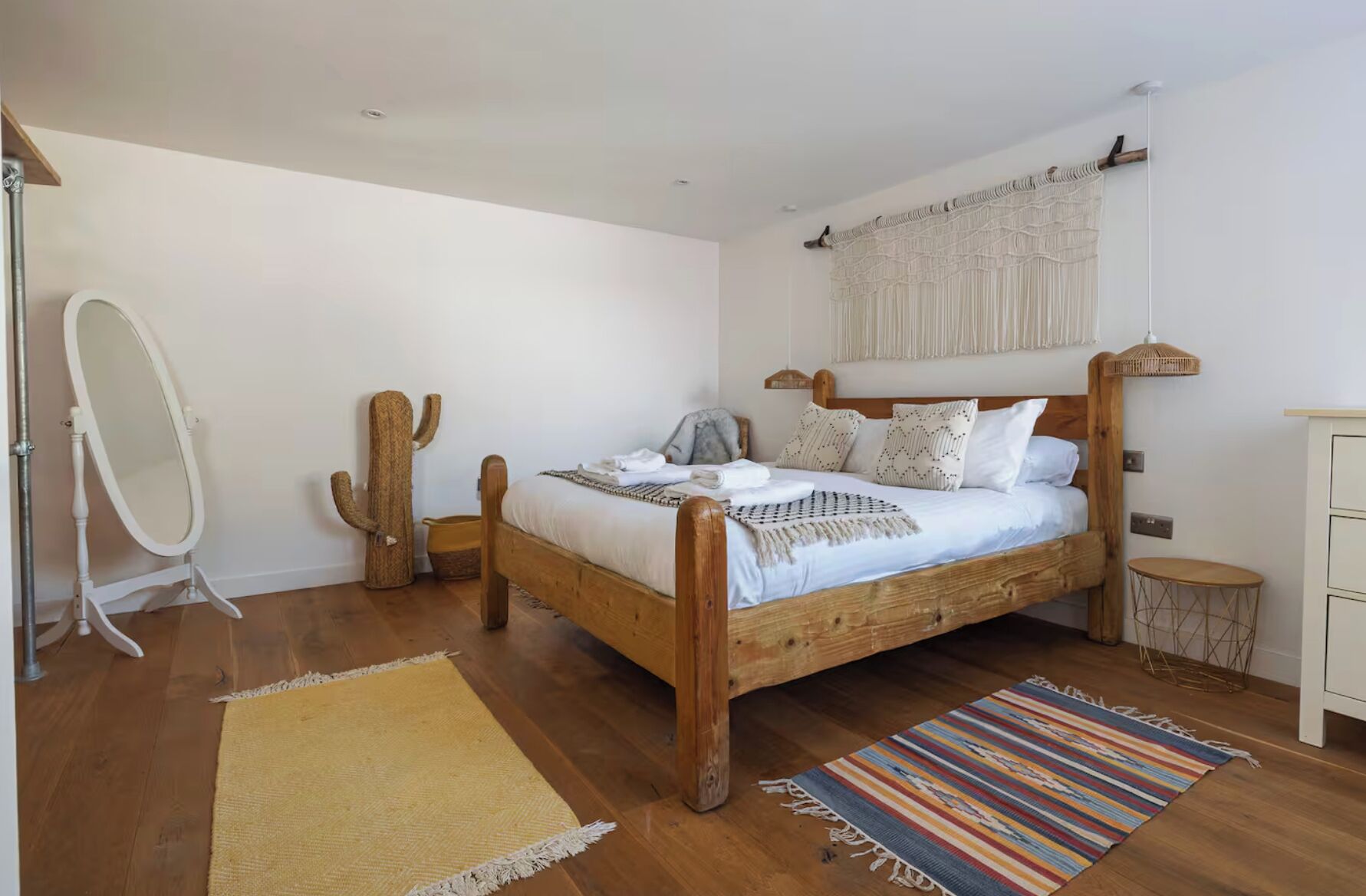 A bedroom with a wooden bed, a small round table, a mirror, and a cactus plant.