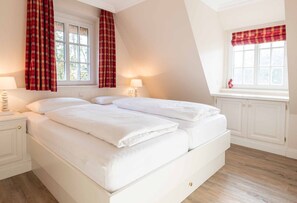 Ein Schlafzimmer mit einem großen Bett, zwei Nachttischen, einem Fenster mit karierten Vorhängen und einer Heizung.